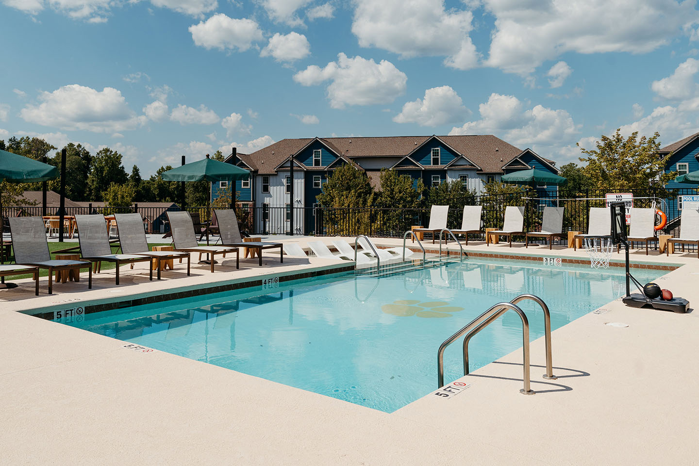 Pool surrounded by lounging chairs and umbrellas with apartment buildings behind it.
