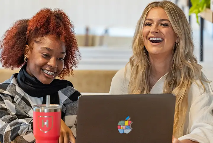 two students smile while working on a laptop